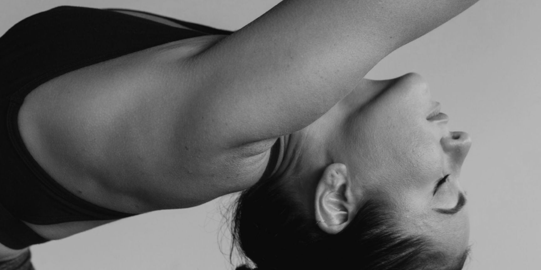 In black and white, a woman bends back with her arm stretched over her head.