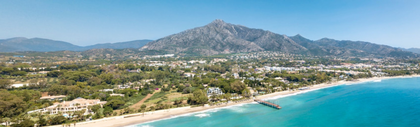 Marbella from the air, La Concha mountain behind the town, the beach, a pier and a turquoise sea.