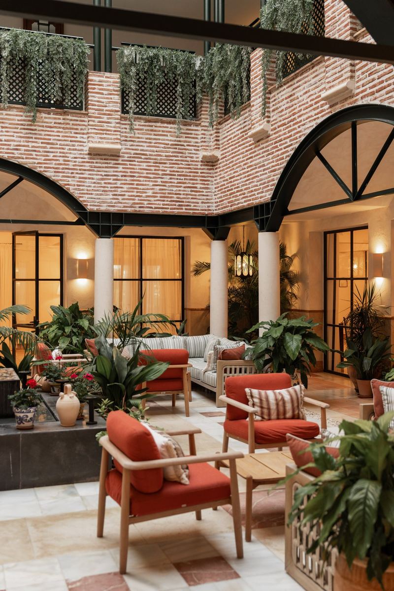 The Gran Hotel Marbella courtyard, brick walls, hanging plants and terracotta armchairs under warm lamps.