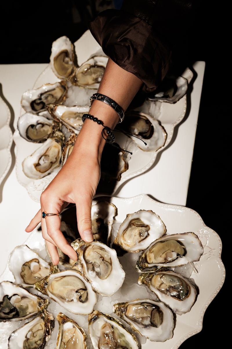 From above, a hand reaches for fresh oysters on white plates.