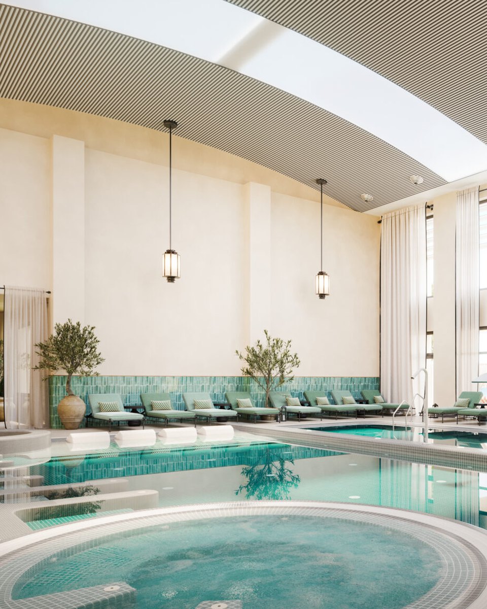 An indoor spa pool with a round jacuzzi under an arched skylight, loungers and olive trees along the wall.