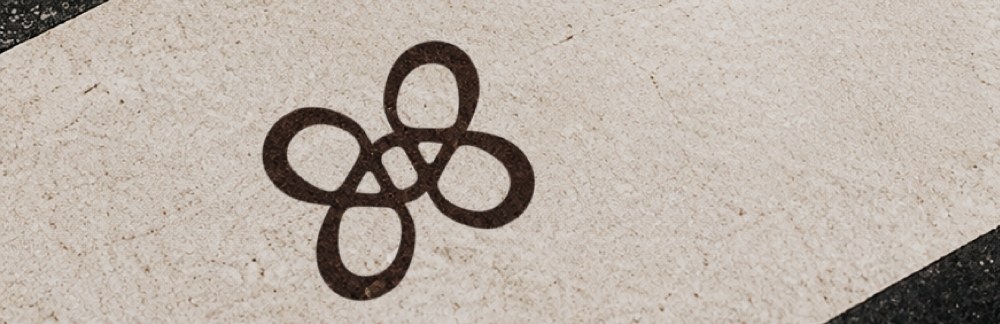 El símbolo de ORIGIN en marrón oscuro sobre una piedra beige con textura.